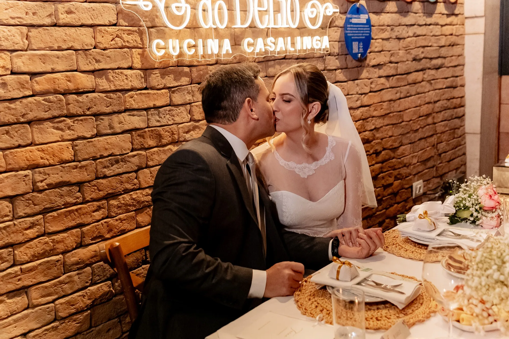 Noivos se beijando à mesa, diante do letreiro da Cantina