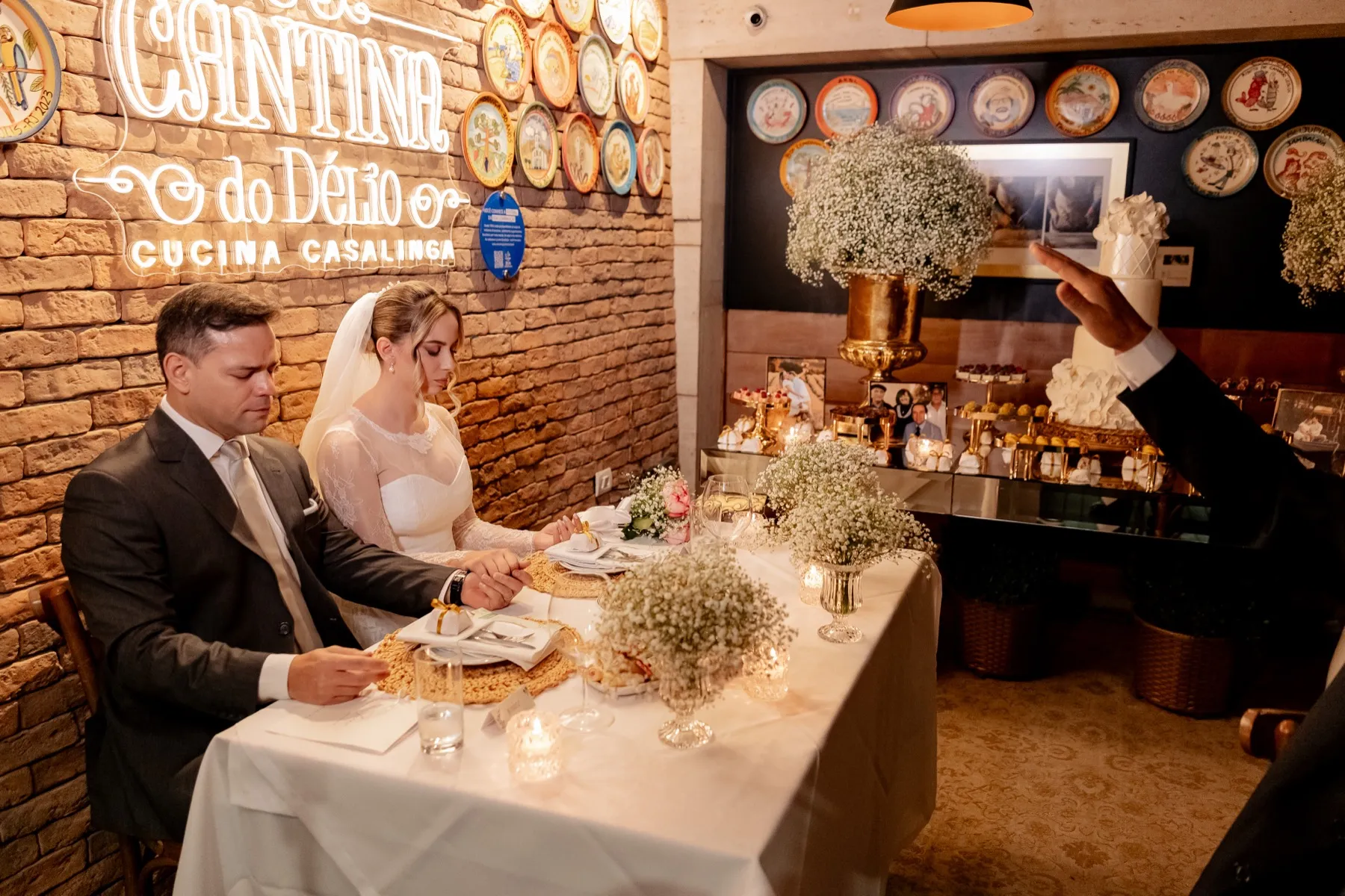 Os noivos à mesa, diante do letreiro da Cantina