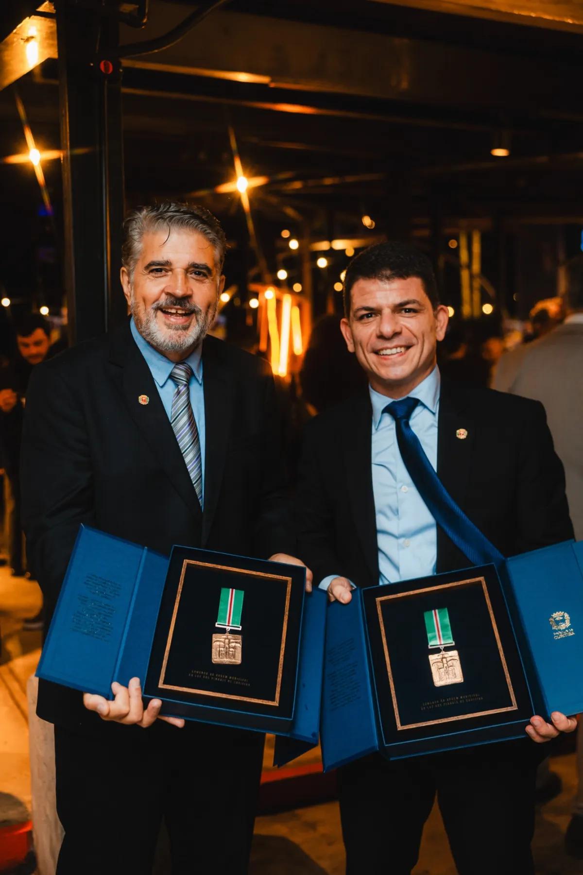 Délio e Bruno Boschilia exibindo as caixas abertas com as medalhas da Ordem da Luz dos Pinhais