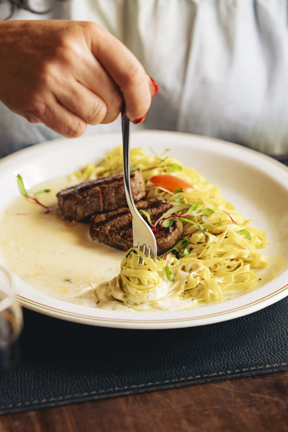Garfo enrolando fettuccine ao lado de um filé